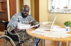 Disabled Veteran US Marine Soldier in Wheelchair. Worried African Veteran in Wheelchair is Looking at Financial Bills at the Home