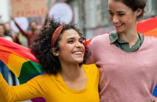 Two young women walk in streets with a pride flag