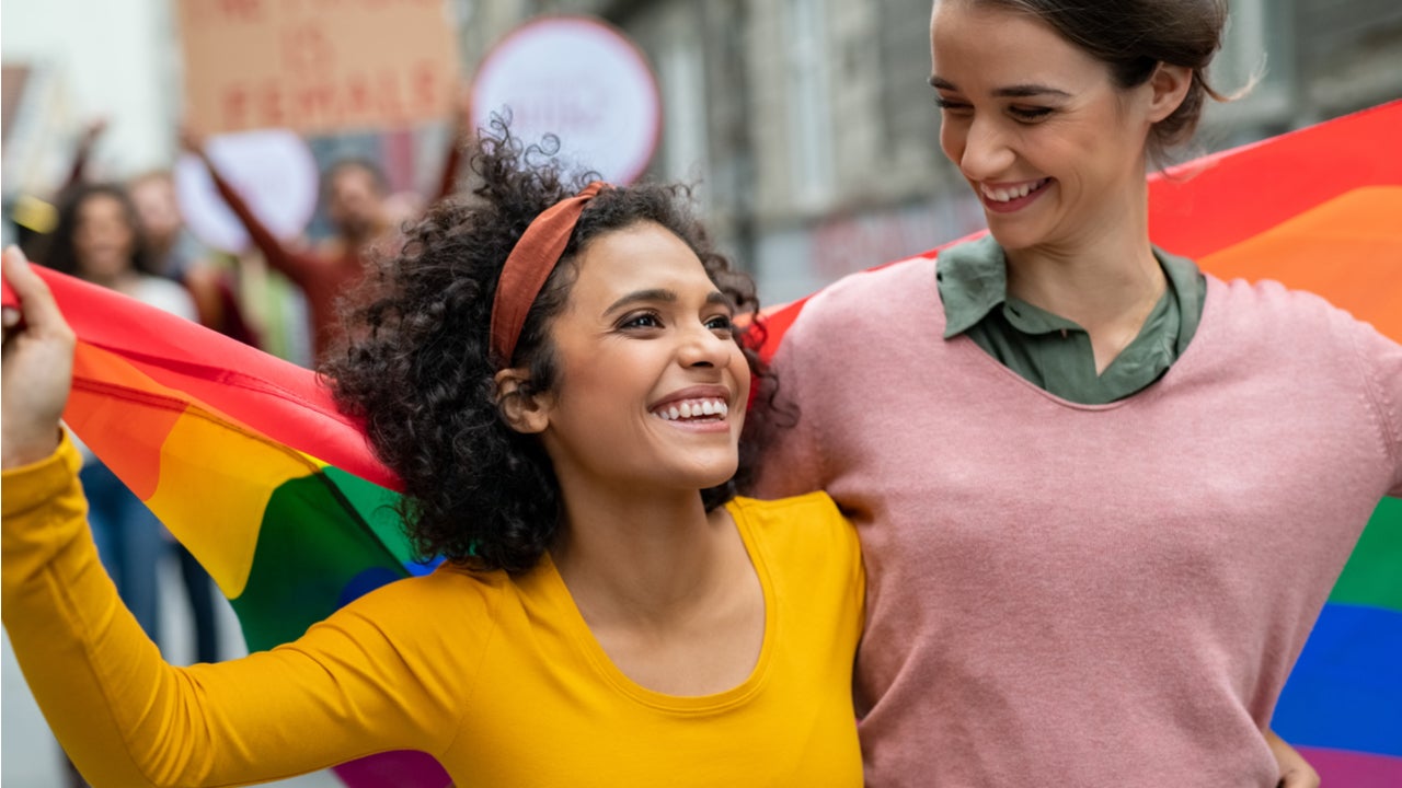 Two young women walk in streets with a pride flag
