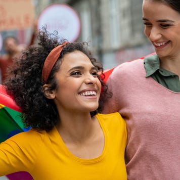 Two young women walk in streets with a pride flag