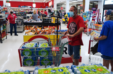 A shopper wearing a protective face mask fills a grocery cart with bottled water at a supermarket.