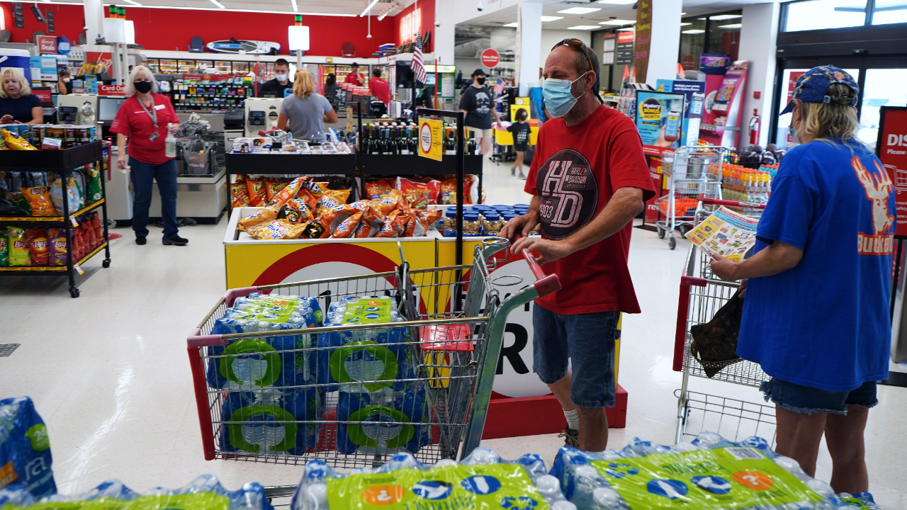 A shopper wearing a protective face mask fills a grocery cart with bottled water at a supermarket.