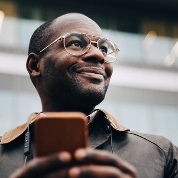 A person with a smartphone smiles and looks into the distance.