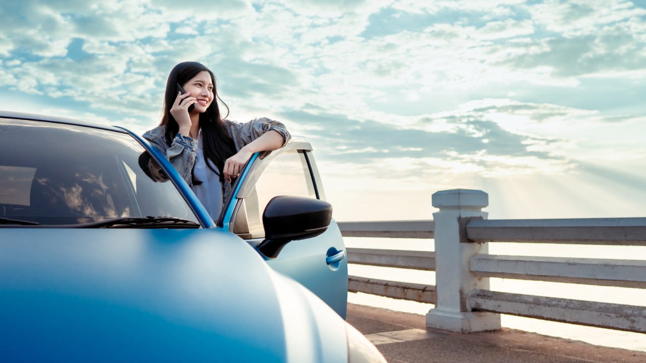 Beautiful teenager asian woman with car travel blue hatchback at beach using smartphone technology enjoy the view happy road trip driving, Freedom people lifestyle in holidays weekend