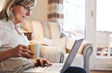 Older woman looking at laptop and holding cup