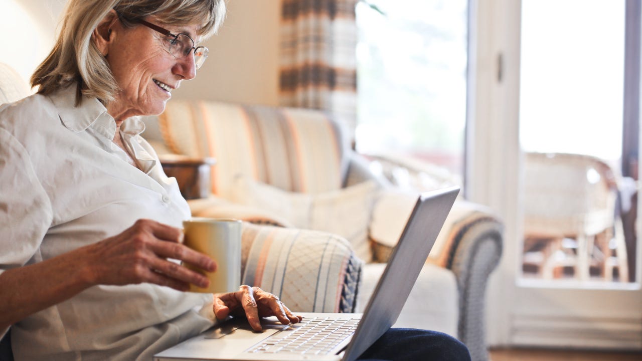 Older woman looking at laptop and holding cup