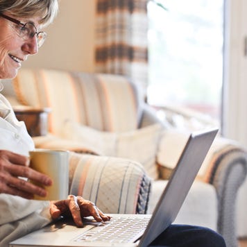 Older woman looking at laptop and holding cup