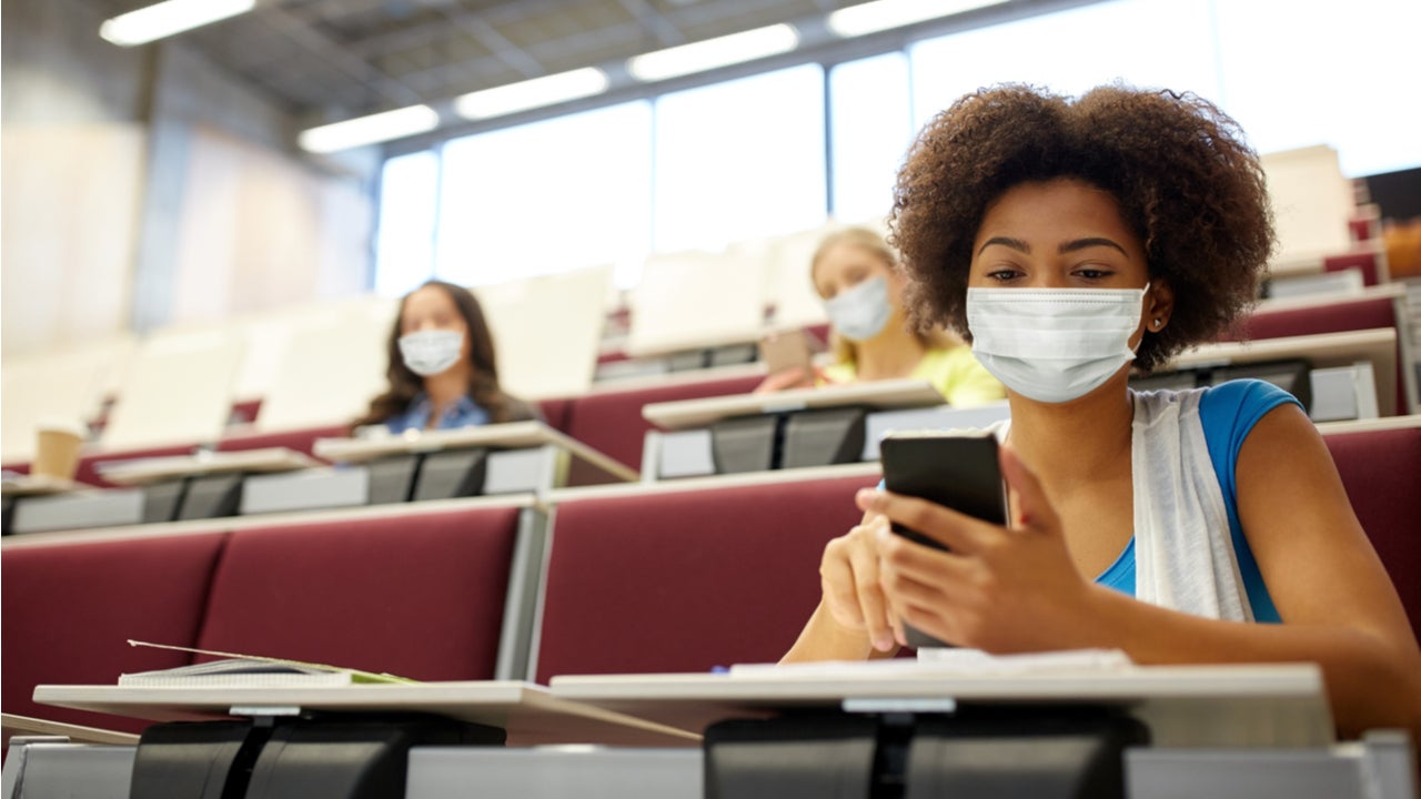 College student sits in a lecture hall with a mask on