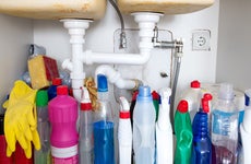 Shot of a cabinet under a sink with cleaning chemicals and products as well as rubber gloves (yellow).