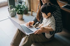 Cropped shot of a young Asian mother using laptop and working from home while taking care of little daughter in self isolation during the Covid-19 health crisis