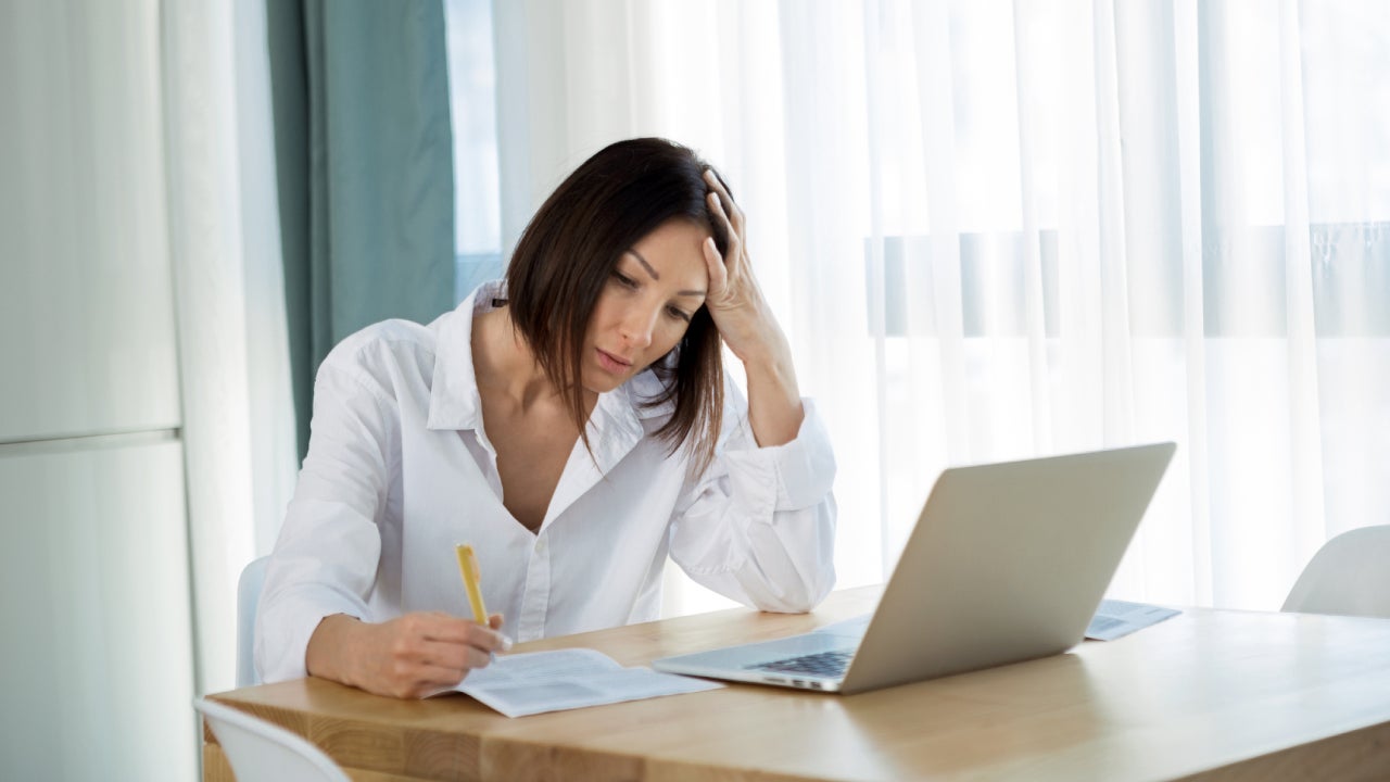 Worried young woman with laptop working from home looking at documents