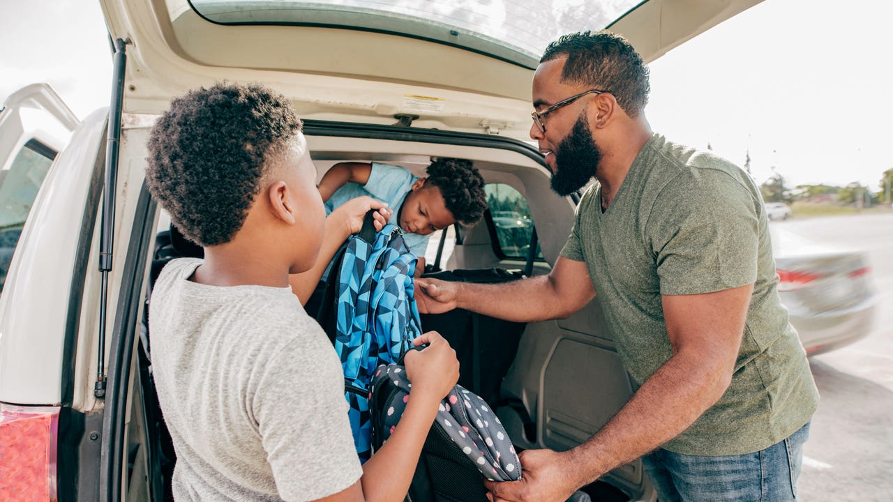 father and two sons getting their backpacks from the car