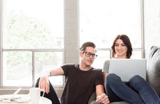 A young couple sits on a couch with their laptop