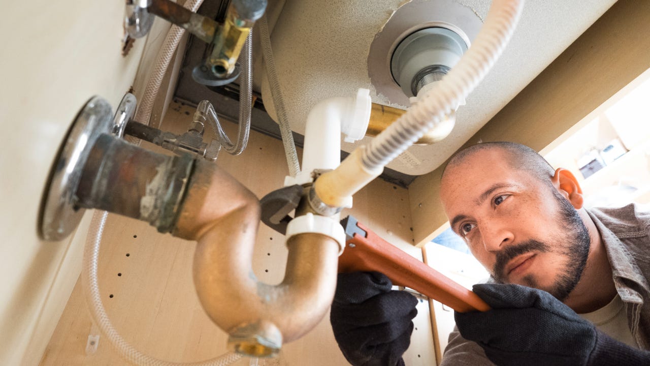 A plumber works under a sink