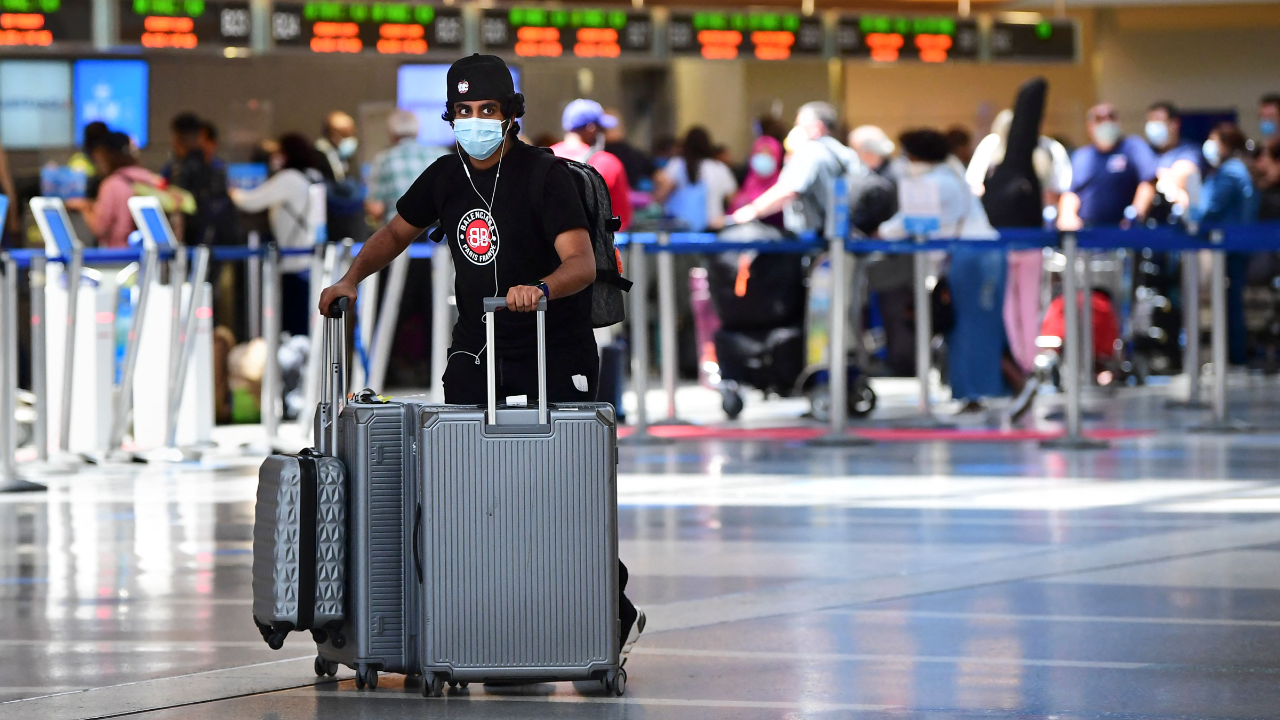 A man pushes his bags on the departures level at Los Angeles International Airport while wearing a mask.