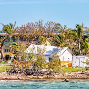 A home on the coast that has been damaged by a hurricane. It is a sunny day.