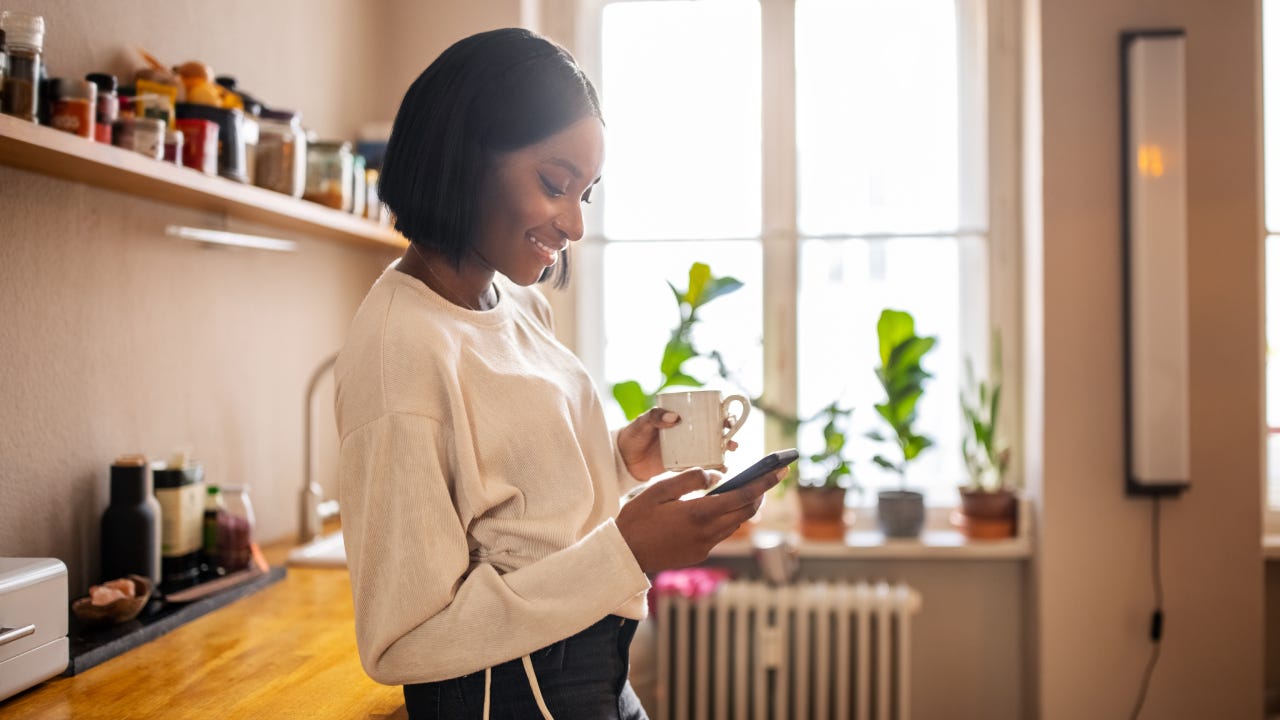 Woman having coffee and texting on her phone at home