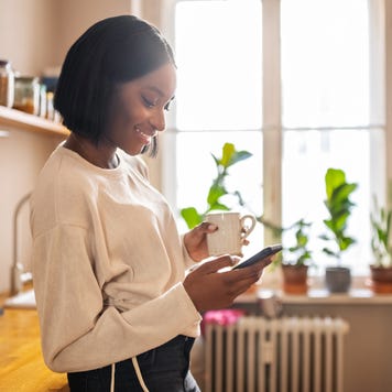 Woman having coffee and texting on her phone at home