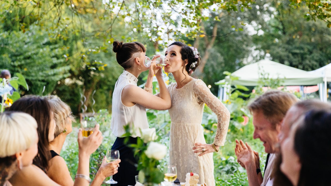 Newlywed lesbian couple drink champagne at reception with friends