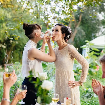 Newlywed lesbian couple drink champagne at reception with friends