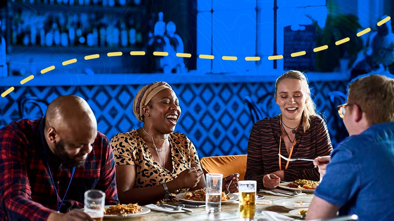 Friends laugh while gathered at a table eating a meal and socialization.