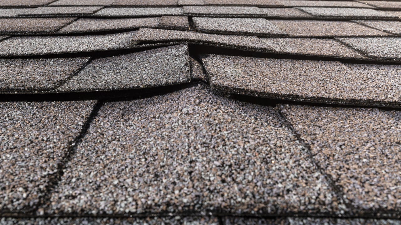 A close-up of a buckled residential asphalt shingled roof