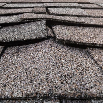 A close-up of a buckled residential asphalt shingled roof