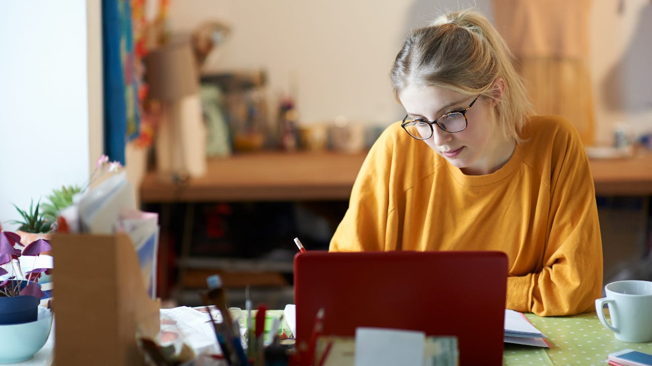 A young woman at home with her laptop making notes