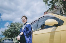 asian chinese young female with graduation gown leaning on her car looking at camera smiling