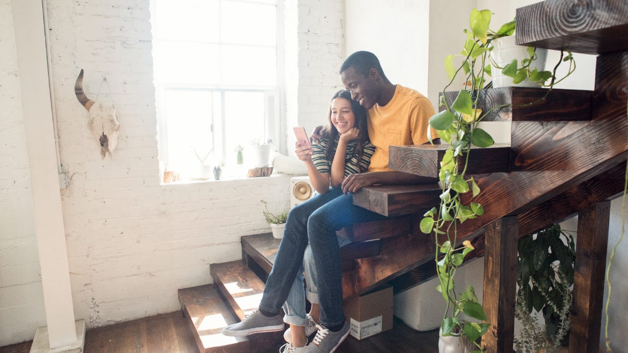 Smiling couple sitting on stairs in a loft sharing cell phone