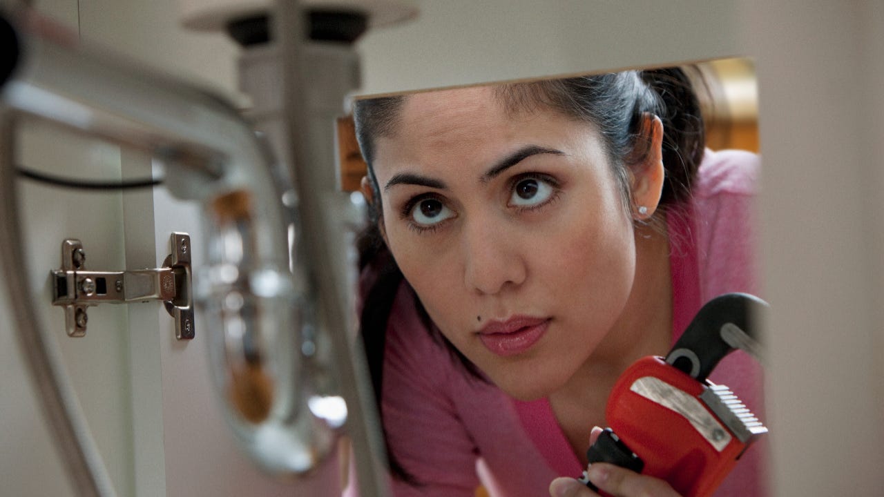 Mixed race woman holding wrench and looking at pipes