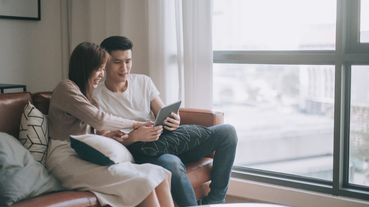 Chinese young couple spending weekend together in living room watching digital tablet