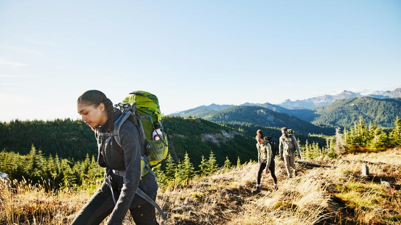 Young woman leading sister and father on backpacking trip