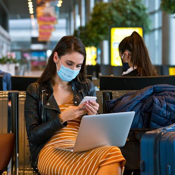 Woman in mask on a smartphone in airport