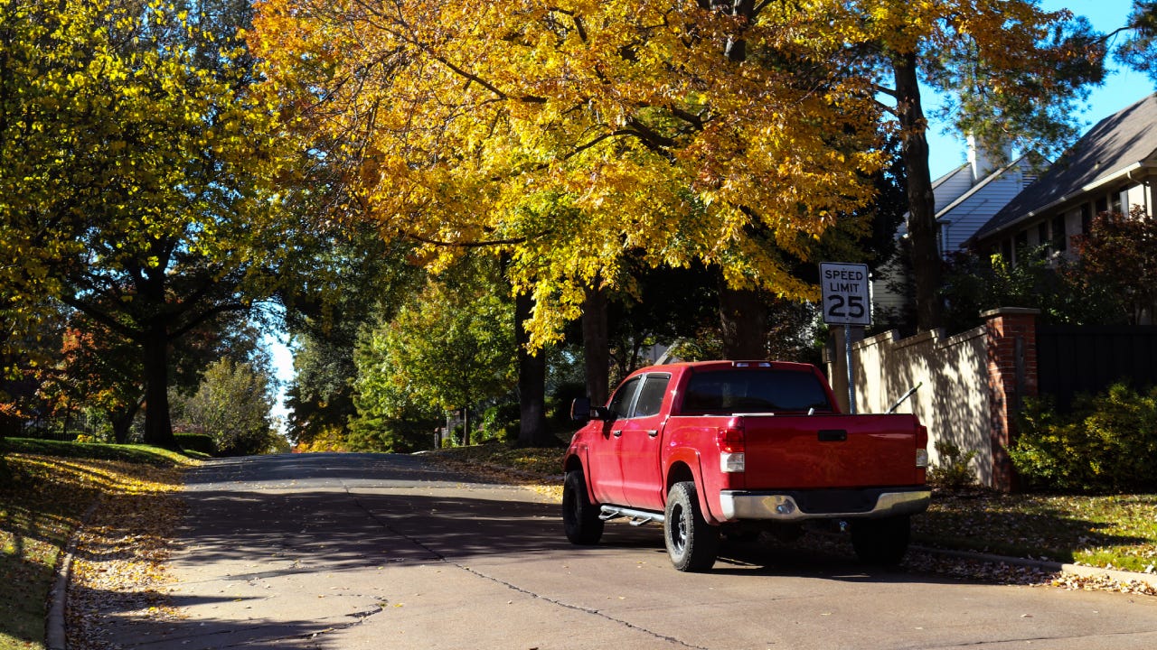 Red pickup truck parked on leafy neighborhood street in Autumn
