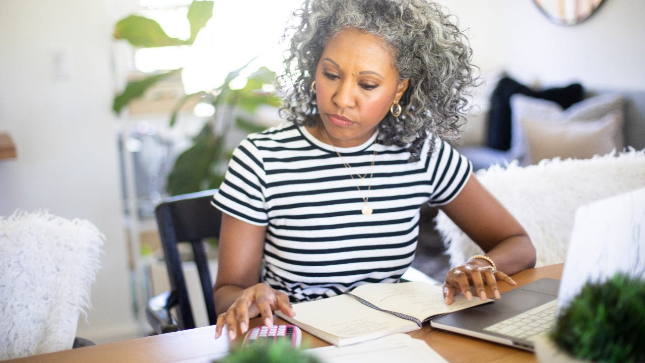 Woman working at home on her laptop with her coffee and a calculator