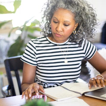 Woman working at home on her laptop with her coffee and a calculator