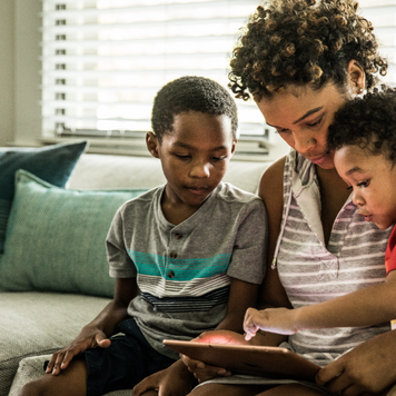 Mother using tablet with young sons on couch