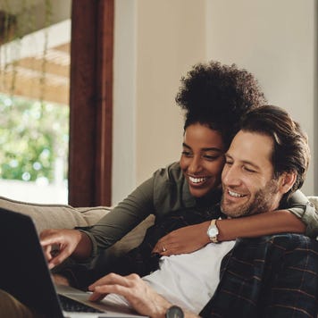 A happy young couple using a laptop while relaxing on a couch in their living room at home