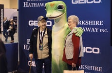 An elderly couple hugging a Geico mascot at Berkshire Hathaway shareholders meeting