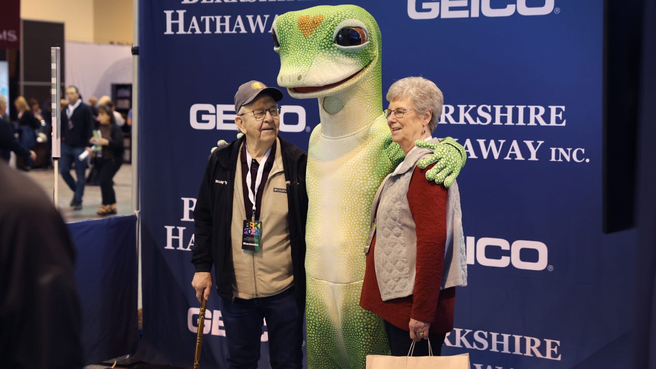 An elderly couple hugging a Geico mascot at Berkshire Hathaway shareholders meeting