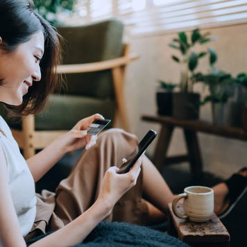 Woman sitting on floor at home shopping online with smartphone while making mobile payment with credit card on hand