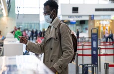 Young man with mask standing at airport ticketing desk