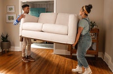 A young couple lifting a couch and moving into a new place.