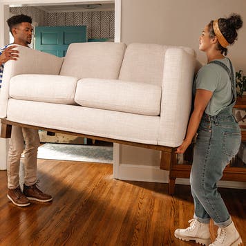 A young couple lifting a couch and moving into a new place.