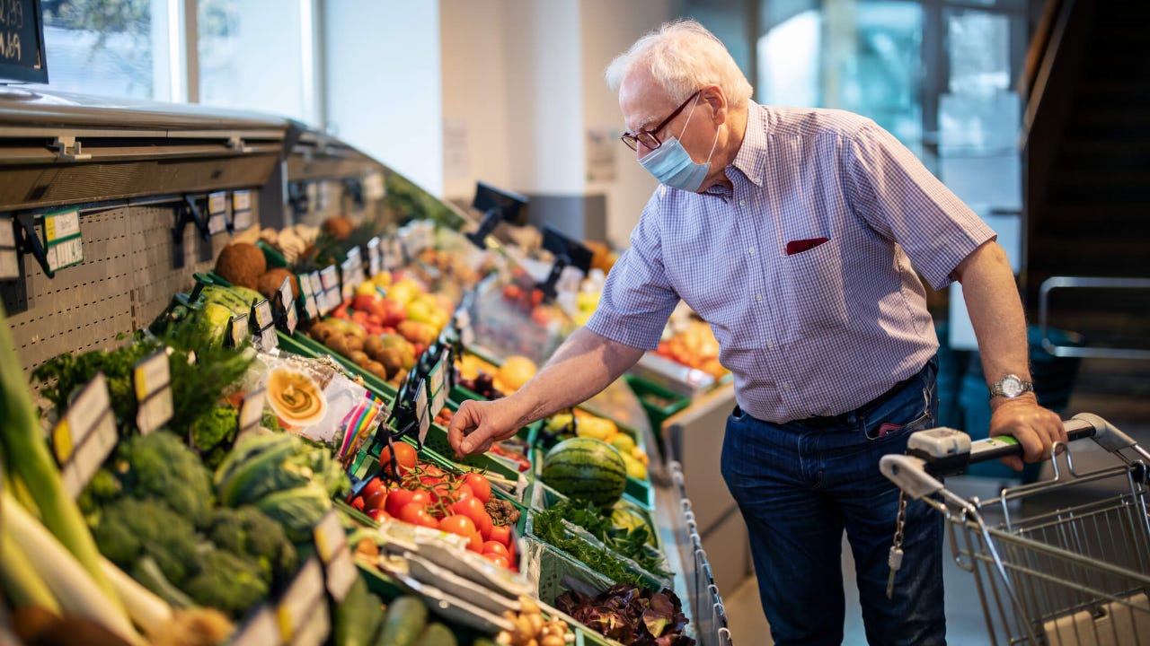 Elderly man with mask browses produce at a grocery store