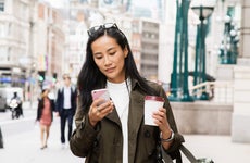 Young woman walks down a city street with coffee while using her smartphone