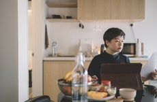 an asian chinese mid adult woman working from home at dining table using digital tablet and documents during breakfast time