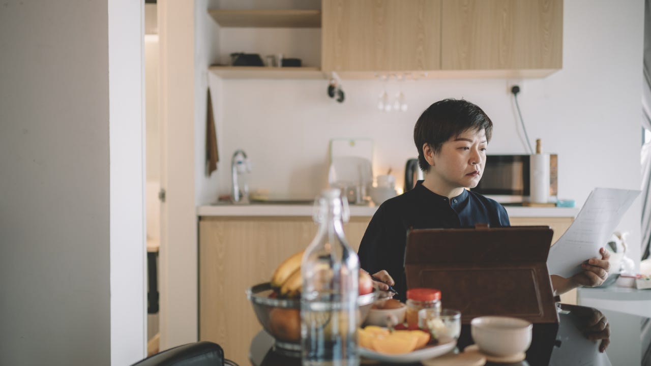 an asian chinese mid adult woman working from home at dining table using digital tablet and documents during breakfast time