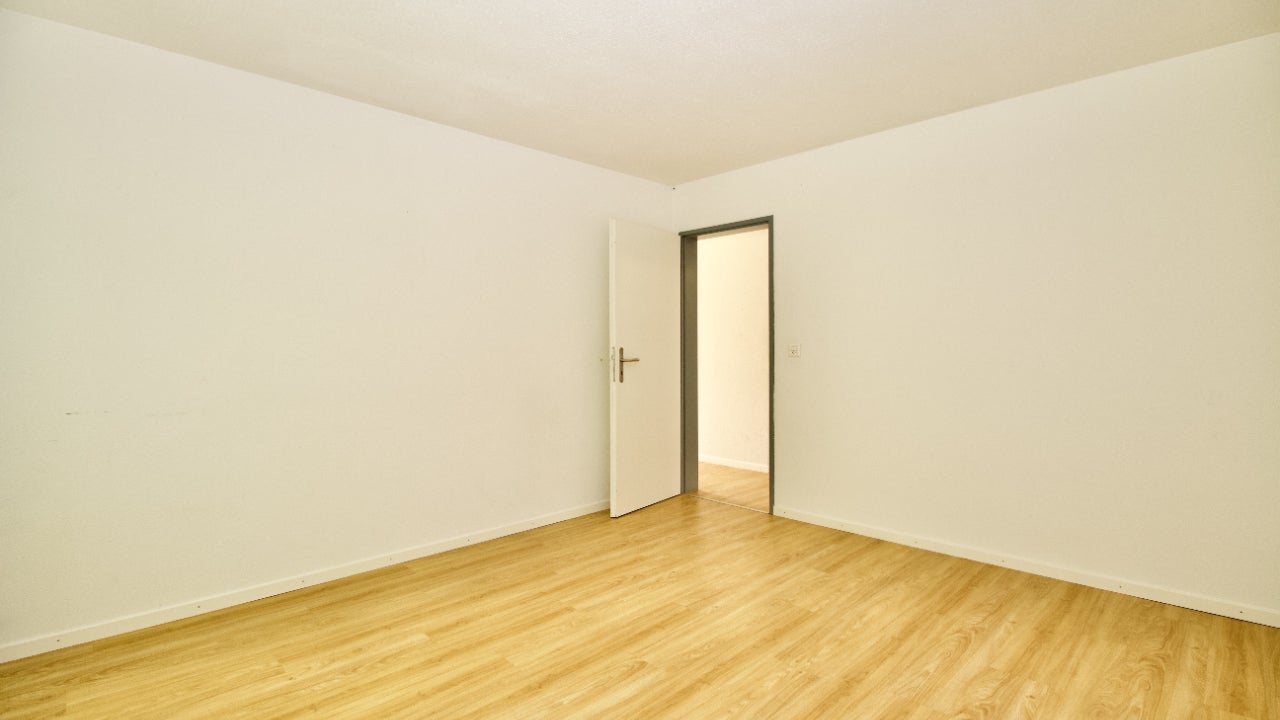 An empty room with light wood floors and white walls